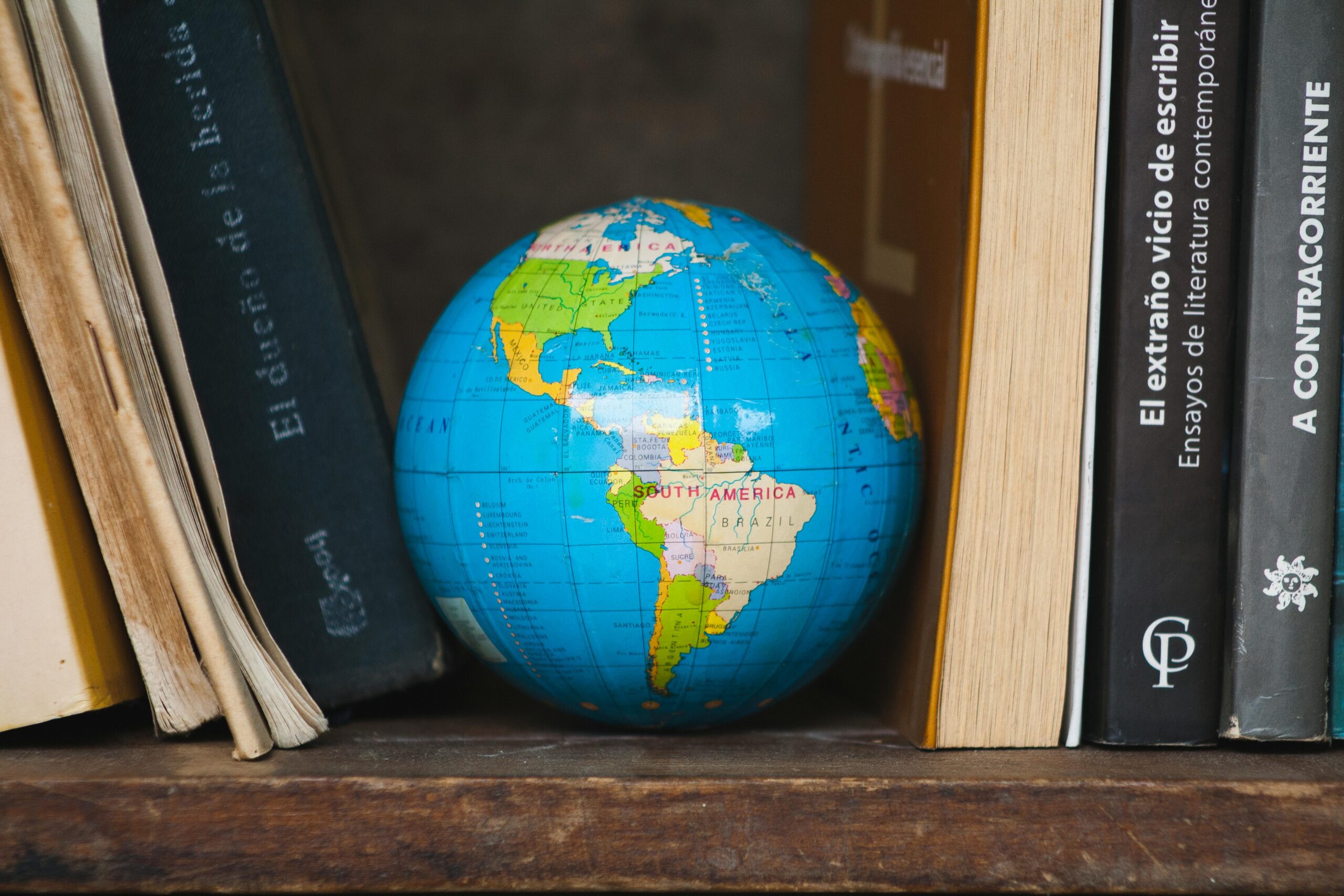 A vibrant globe nestled between classic books on a wooden shelf, highlighting South America.